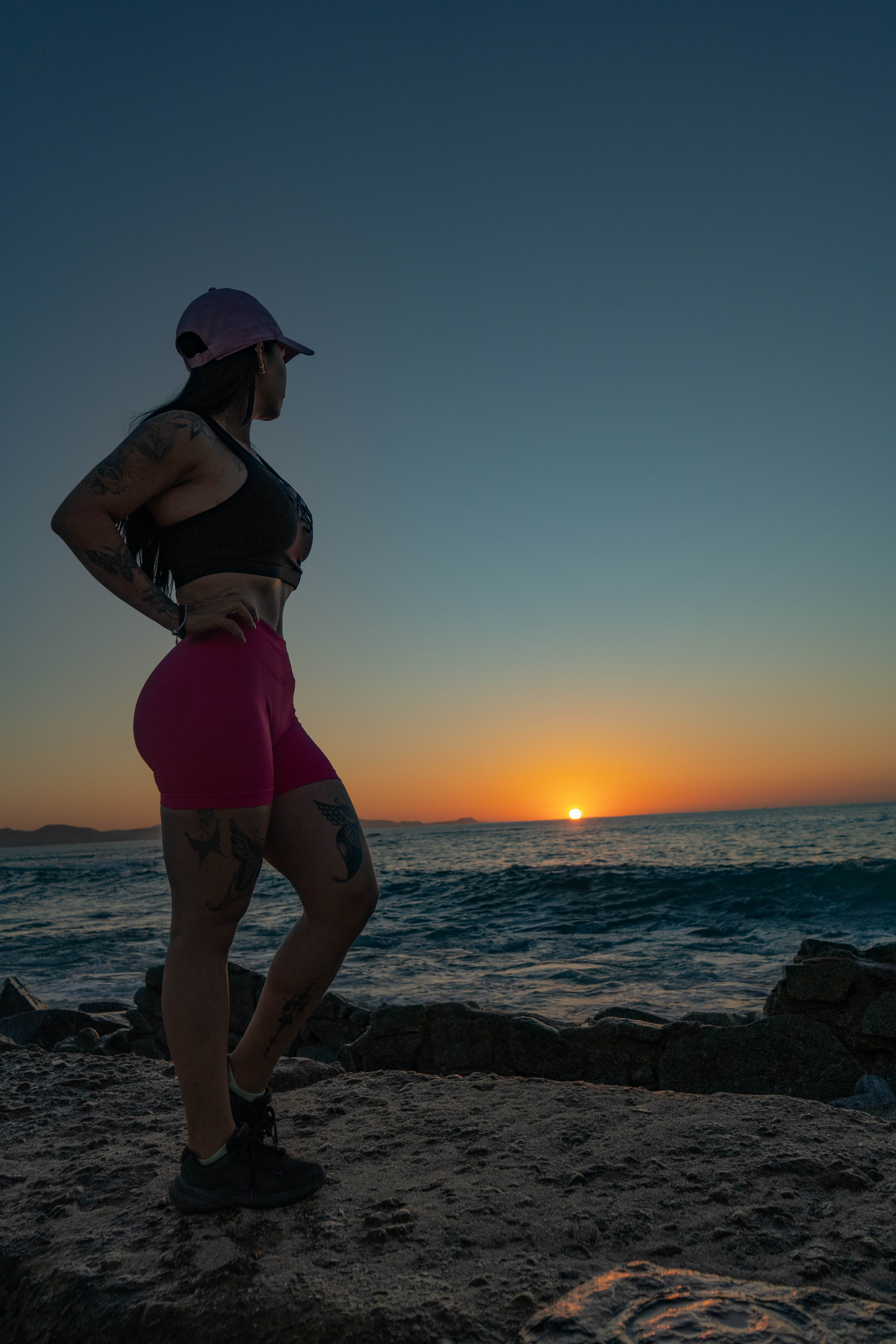 Silueta de Patricia en rocks al atardecer, manos en la cadera