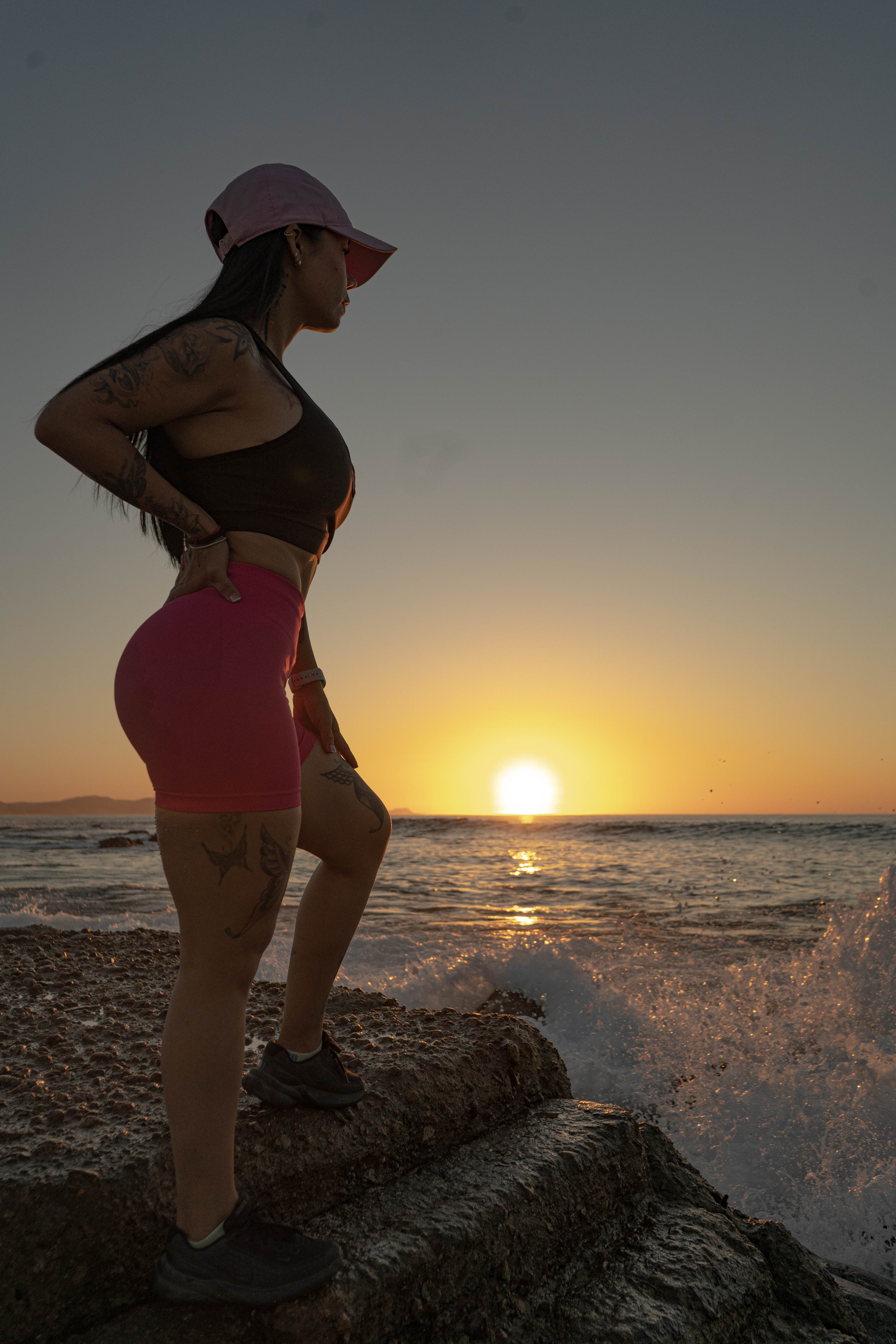 Silueta atlética sobre las rocas al atardecer con salpicadura de ola