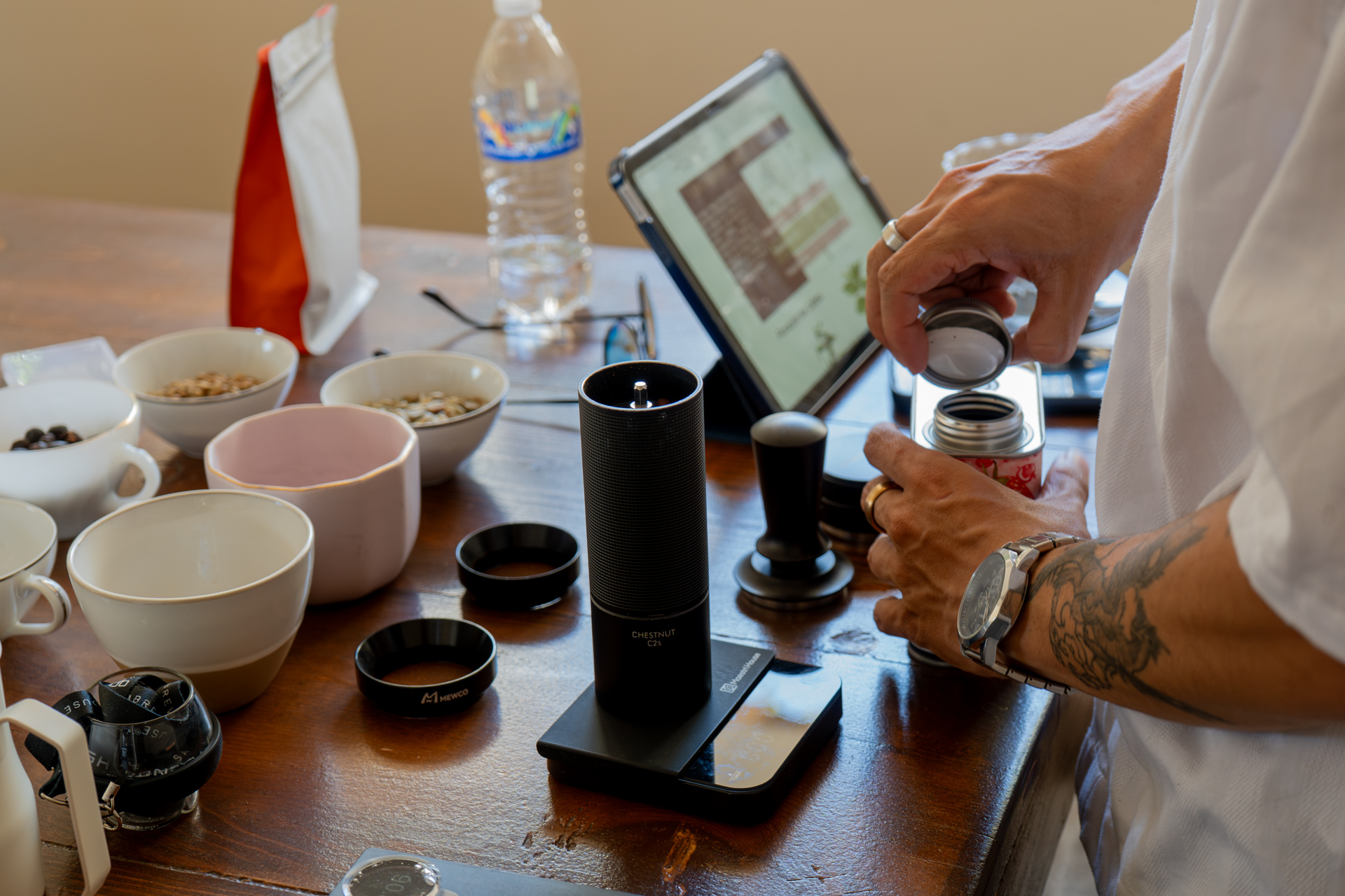 Molino de madera entre manos tatuadas y tablet sobre la mesa